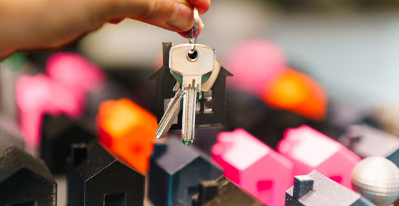 Photo of hand holding a pair of keys above small, miniature models of houses